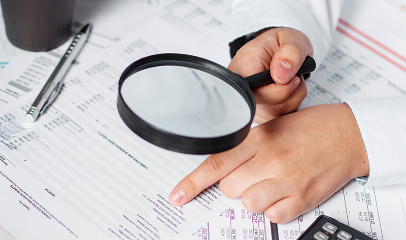 Businessman using magnifying to review balance sheet annual