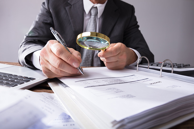 Man in suit looking over paperwork with a magnifying glass