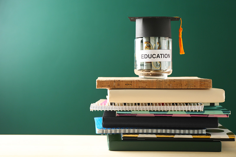 Education written on a jar full of cash money and sitting on a stack of notebooks