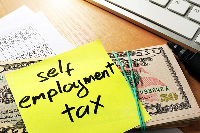 Self Employment Tax written on a sticky note stuck to a stack of money