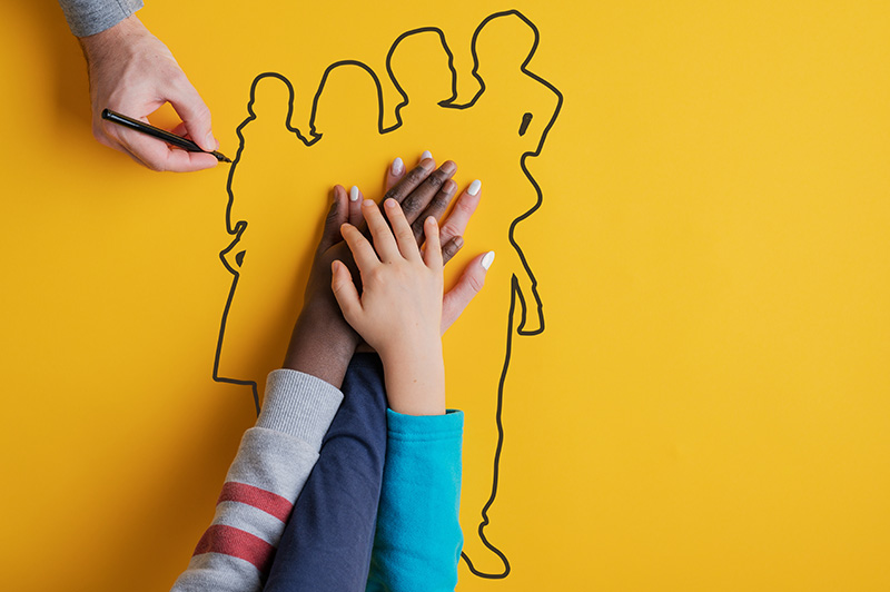 Hand drawing of a family on yellow paper with 3 hands reaching on top